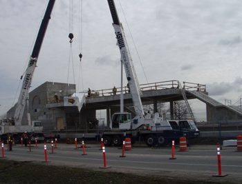 An escalator is delived and installed by two overhead cranes.