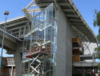 Workers install glazing on the glass-enclosed staircase tower.